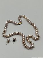 Front view of cultured pearl necklace and matching stud earrings laid flat