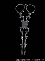 Front view of scissor-style sugar tongs against black background