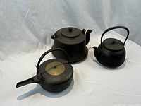 Overview of three cast iron sake kettles with varying shapes and sizes