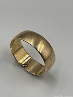 Angled side view of the gold band ring showing domed profile and surface wear.