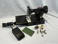 Overall lot: sewing machine on base, foot pedal, instruction booklet, presser feet and accessories arranged in front