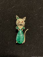 Front view of a vintage gold tone cat-shaped brooch with red, emerald, and jade colored stones.