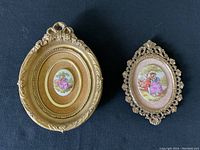 Two framed vintage Limoges porcelain cameo medallions side by side on a dark surface showing gold-toned frames and painted porcelain scenes.