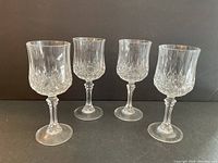 Four clear crystal wine glasses with decorative textured pattern and stems, shown on black background.
