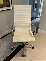 Front view of white faux leather office chair showing horizontal ribbed upholstery and some flaking at the front of the seat, metal armrests, and metal 5-star base with casters.