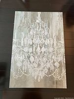 Front view of chandelier art print laid flat on dark wood floor showing entire artwork and details of print and texture.