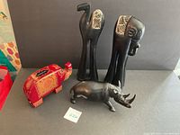 Four animal figurines including a red leather elephant bank, black wooden camel and elephant statues, and a heavy rhinoceros figurine on a black surface.