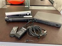 Three DVR units (NVR, Invezio, FLIR MPX), power adapter, remote and cables on table