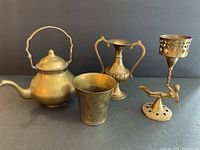 Full view of all four brass items together against dark background