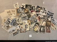 A spread of medium-sized vintage photographs on a surface, showing different portrait and candid photos of men, women, and children mainly in black and white and sepia tone.