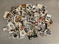 Top view of a large scattered pile of vintage black and white and color photographs featuring people and various scenes on a gray floor.