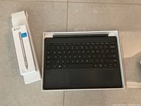 Microsoft Surface Pen box unopened next to Surface Pro keyboard inside its original box.