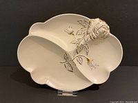 Full view of the cream-colored decorative platter with prominent raised rose and leaves, showing its shape and detailing.