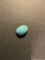 Top and angled views of a turquoise oval cabochon stone on dark and light backgrounds.