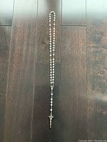 Full view of the 18-inch mother of pearl rosary with metal links, centerpiece, and crucifix on dark wood floor.