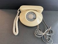 Beige Northern Telecom rotary phone with coiled handset cord and telephone cable, placed on dark surface.