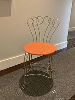 Front view of vintage vanity stool showing round peach vinyl seat and gold tone metal frame with decorative curved backrest.