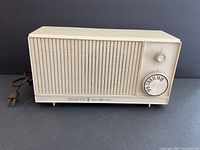 Front view of beige Zenith radio showing speaker grille, tuning dial marked with frequencies, and control knob.