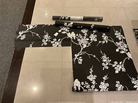 Photo showing one unopened full roll, one nearly full roll, and four partial pieces of black wallpaper with white branches, birds, and cherry blossoms pattern.