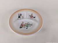 Full top view of divided porcelain plate with orange rim and three sections illustrated with children playing and toys.