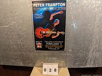 Poster pinned on a wall with a number card in front showing '028', displaying Peter Frampton playing guitar for the Lynn Auditorium concert on February 3.