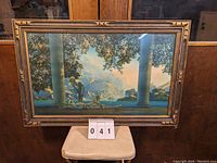 Full frontal image of framed Maxfield Parrish print titled "Daybreak" showing figures, column and landscape in a bronze-gold decorative wooden frame.