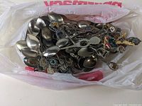 Photo of a plastic bag full of various souvenir spoons with different designs and colors on their handles.