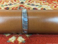 Silver Navajo bracelet displayed on brown leather stand with a carved linear patterned band