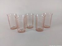 Set of five pink depression glass tumblers arranged in a row on a white surface, showing full height and shape