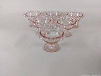 Six pink depression glass sherbet dishes arranged in a triangular formation with one in lower front and five behind, showing the shape, pattern, and detail of the dishes.