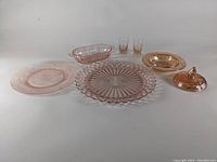 Wide shot showing seven pieces of depression glass including various plates, shot glasses and covered dish, laid out side by side.