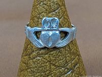 Front view of the sterling silver Claddagh ring resting on a brown textured cone display, showing the heart, hands, and crown design clearly.