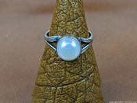 Front view of sterling silver ring with a round white cultured pearl mounted in a bezel setting, displayed on a textured ring stand.