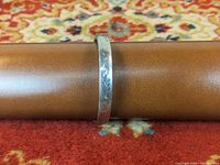 Sterling silver bangle bracelet showing detailed floral engraving on the outer front surface with reflective silver finish.