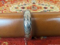 Close-up of sterling silver bangle showing engraved tulip flower and leaf pattern on outer surface.