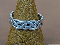 Front angle showing continuous knotwork design on sterling silver ring on a textured display stand.