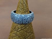 Sterling silver ring band with pebbled surface displayed on ring holder, showing front side of the ring and texture details.