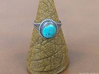 Front view of sterling silver ring with turquoise stone on a brown textured display cone