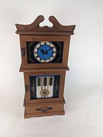 Front view of the wooden music box shaped like a grandfather clock, showing clock face, piano keyboard design, and bottom drawer with handle.