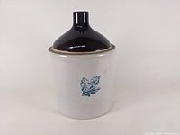 Front view showing the light beige body with a small blue leaf emblem and glazed dark top with spout