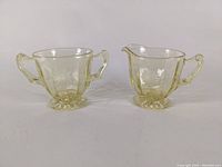 Front view showing the creamer with spout and single handle, and sugar bowl with two handles on opposite sides, highlighting the etched designs and yellow tint.