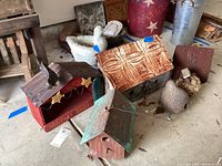 Photo showing multiple decorative birdhouses and feeders arranged on the floor, including a green roof birdhouse, red metal feeder, and items with rusted metal and wood.