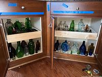 Two wooden cabinets with glass bottles in a pull-out tray and bottom compartment showing various colored bottles.