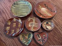 Overview of seven folk style redware pottery pieces showing various patterns, shapes, and sizes from 4-9 inches diameter, including round and heart-shaped pieces.