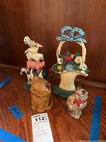 Photo showing all four cast iron items including the cat bank, stacked animal doorstop, and floral basket doorstop, placed on wooden surface.