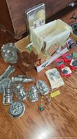 Overview of various cookie cutters and molds on a wooden floor including shaped molds and a cloth-lined box with small packaged items.