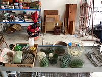 Wide shot of grey metal shelf with cardboard box holding assorted flower frogs and two grey metal basket frames on right
