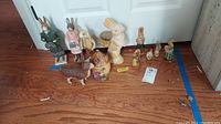 All figurines on wood floor: 2 tall rabbits, white planter, donkey, house box, small chicken, gold rabbits, small carved bunnies