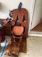 Overall composition showing the tall carved and hand painted wooden pumpkin decoration with a blue price tag, metal decorated bucket, and smaller hand painted pumpkin decorations with Halloween theme.
