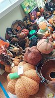 Photo showing fabric pumpkins, Halloween figures, a pumpkin faced metal bucket and a variety of other Halloween decor items on a table.